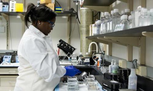 A woman in a lab, wearing a white lab coat 和 gloves. 